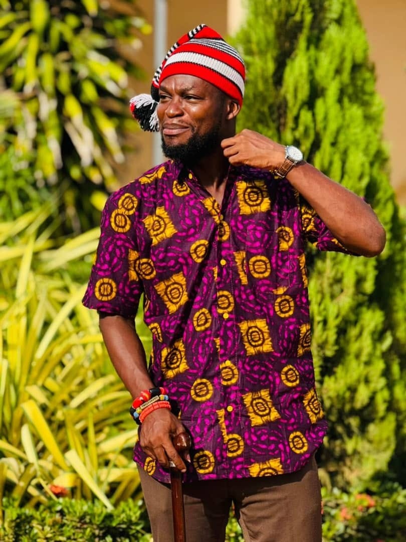 Wugah Shaddrack Selali wearing a patterned shirt and a red, black and white hat outdoors